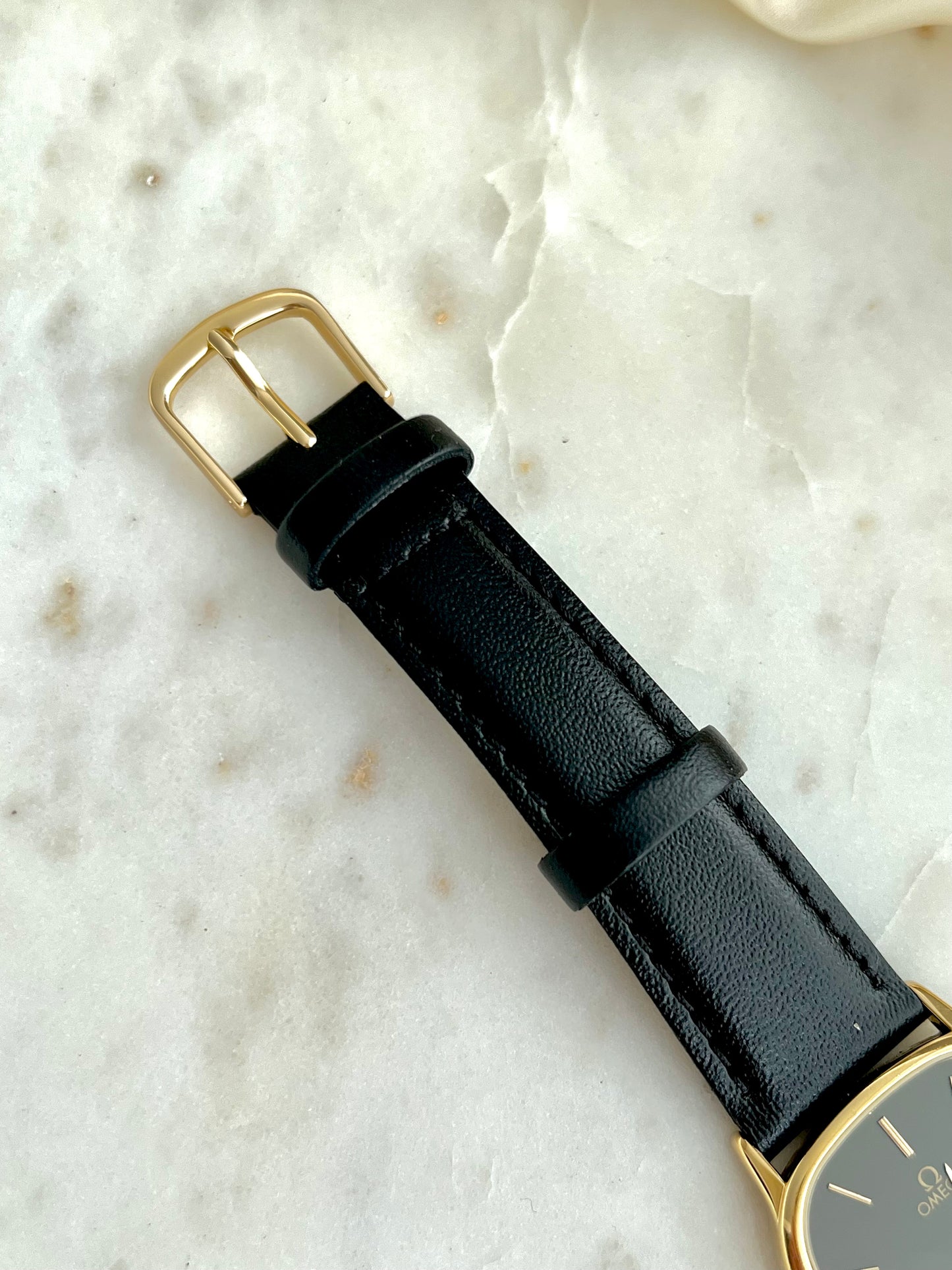 Black leather watch strap with gold buckle on a light marble background