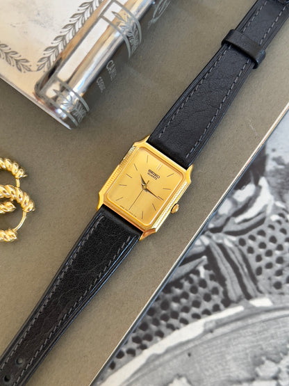 Gold watch with black leather strap on a textured surface