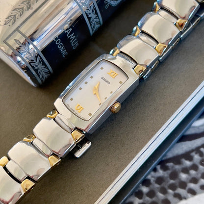 Silver and gold watch on a textured surface with a book in the background