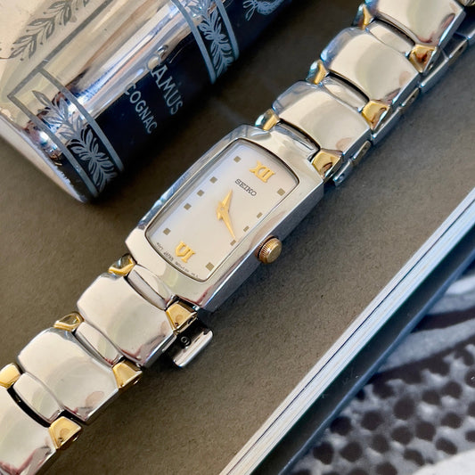Silver and gold watch on a textured surface with a book in the background