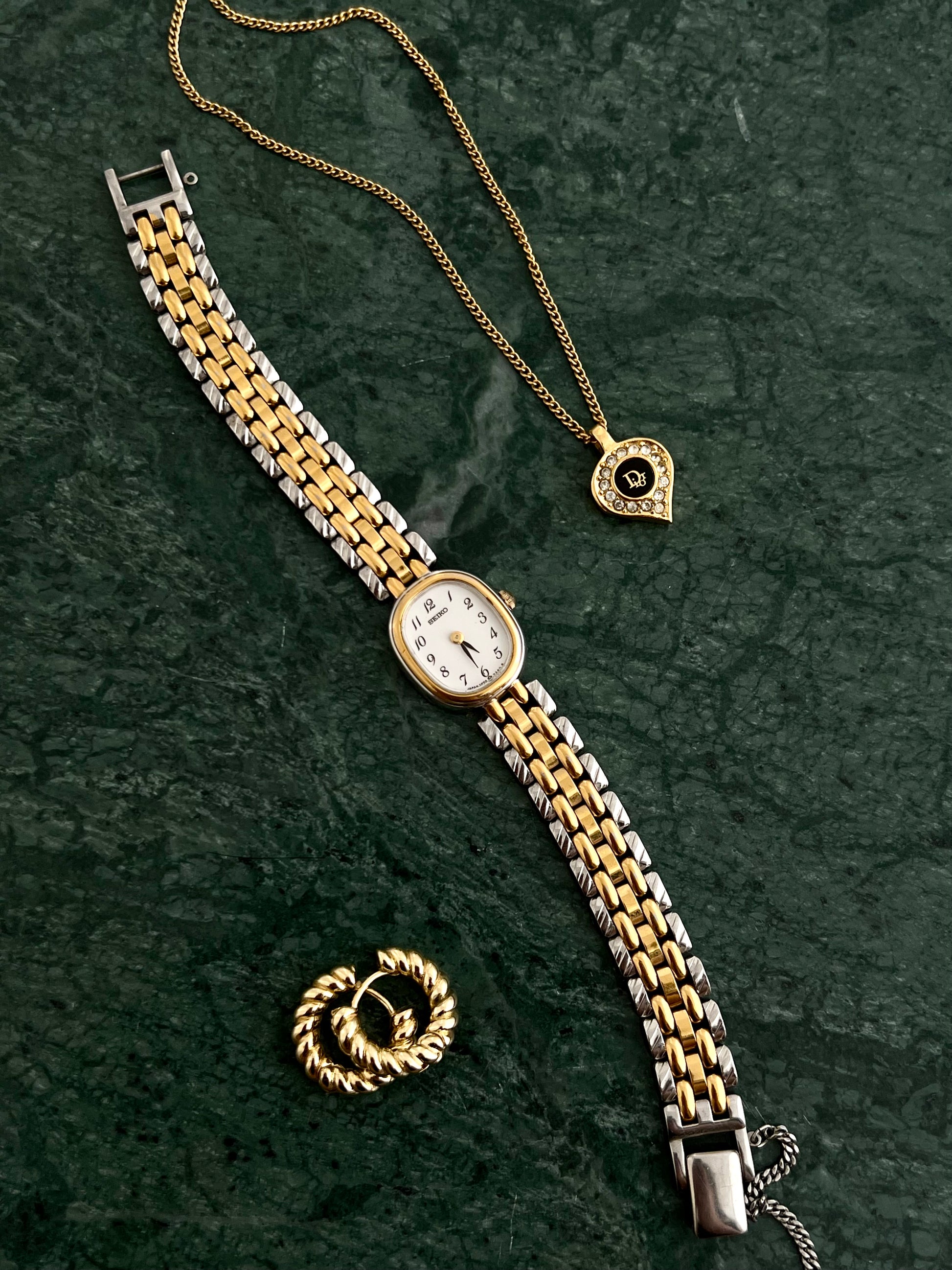 Gold vintage Dior heart pendant necklace with diamond detailing styled on green marble, and Seiko women's watch feminine jewellery aesthetic photographed by The Gilded Hour NZ.