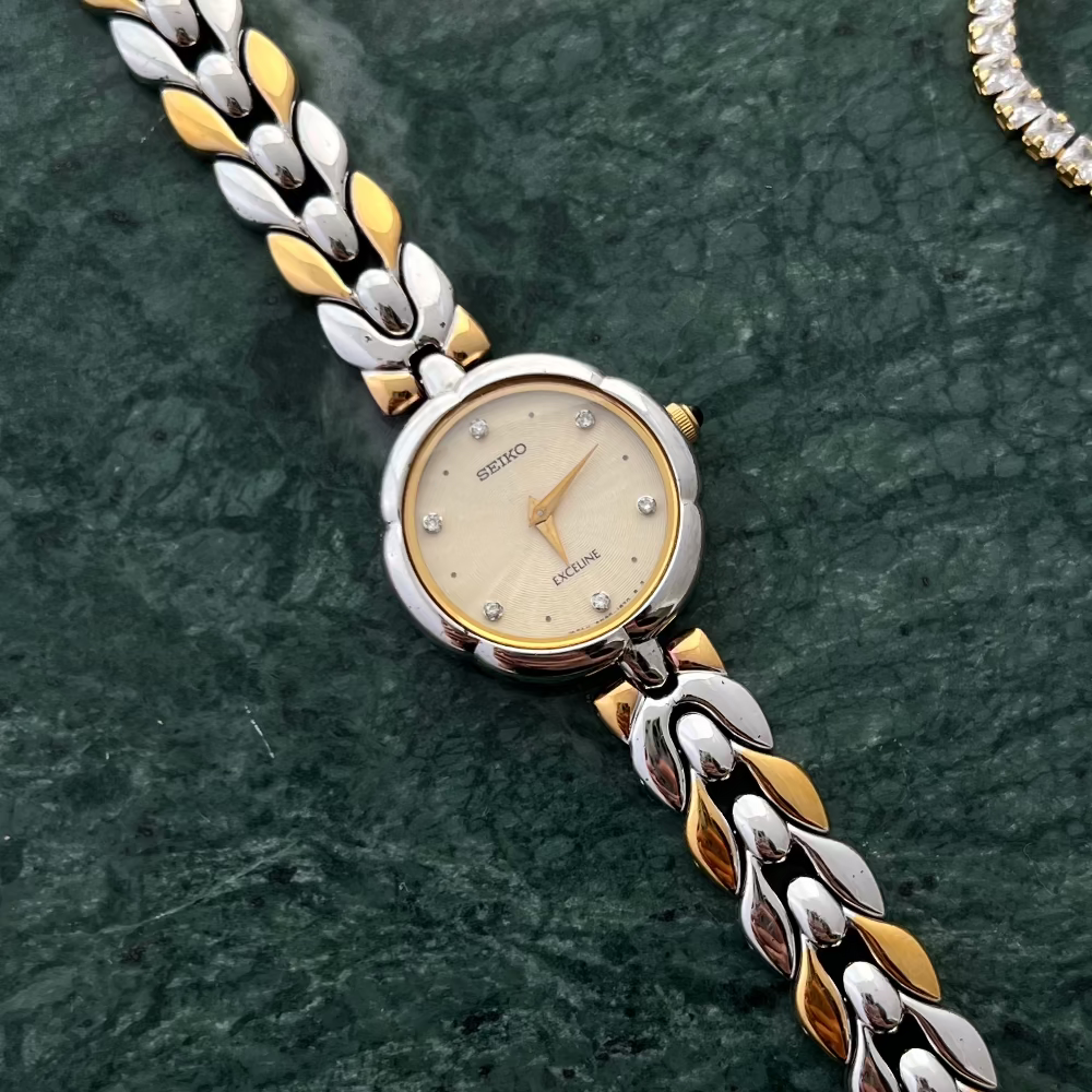 Seiko Exceline Woman's watch with a silver and gold braided strap on a dark green background