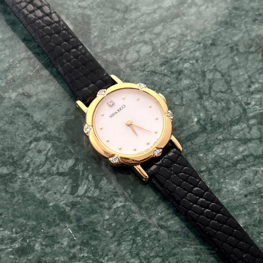 Nina Ricci Gold watch with a black strap on a green marble surface