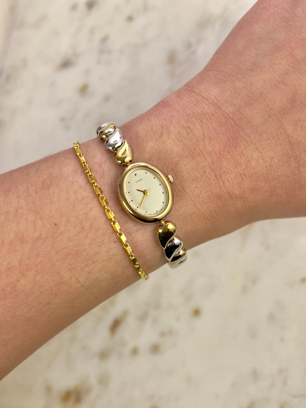 Gold watch and bracelet on a wrist with a neutral background