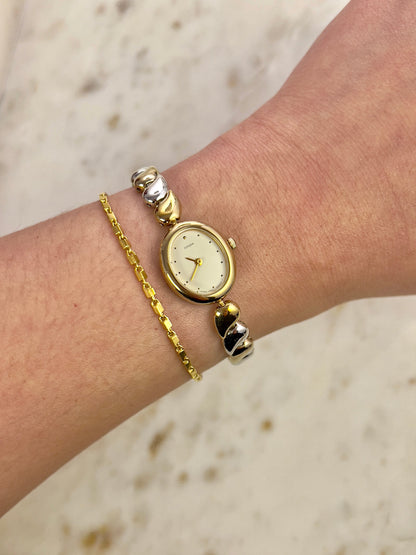 Gold watch and bracelet on a wrist with a neutral background