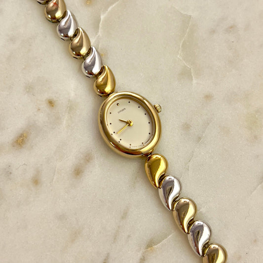 Citizen gold and silver beaded bracelet with a watch face on a marble surface