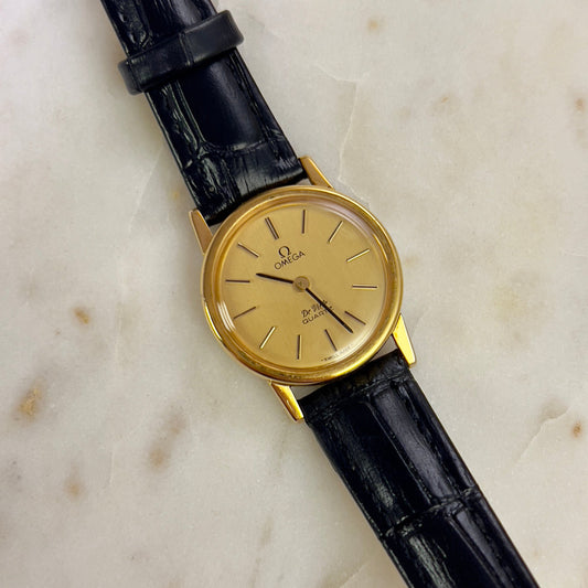 Omega gold ladies watch with black leather strap on a marble surface