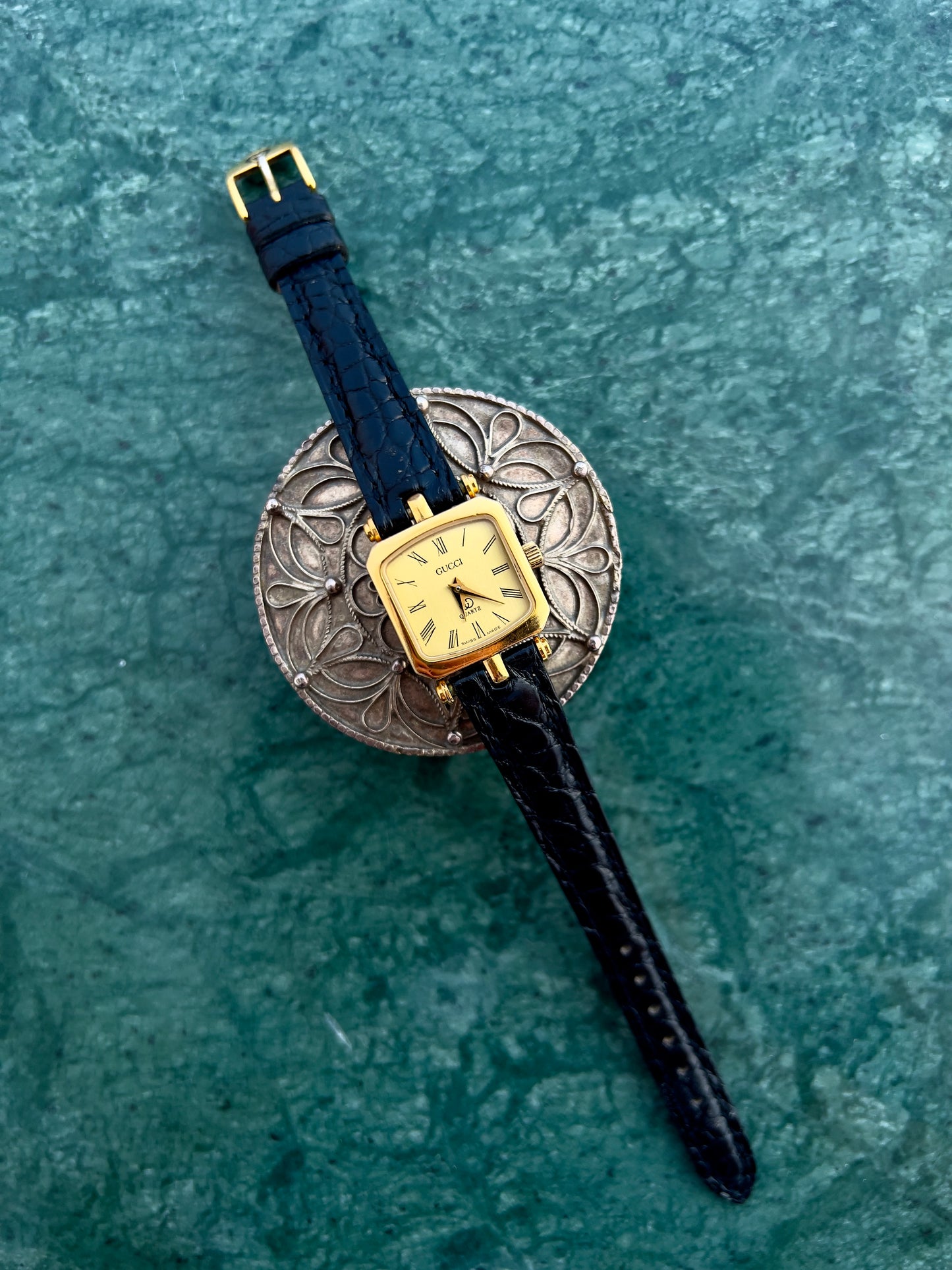 Gucci Wristwatch with gold case and black strap on a textured green surface