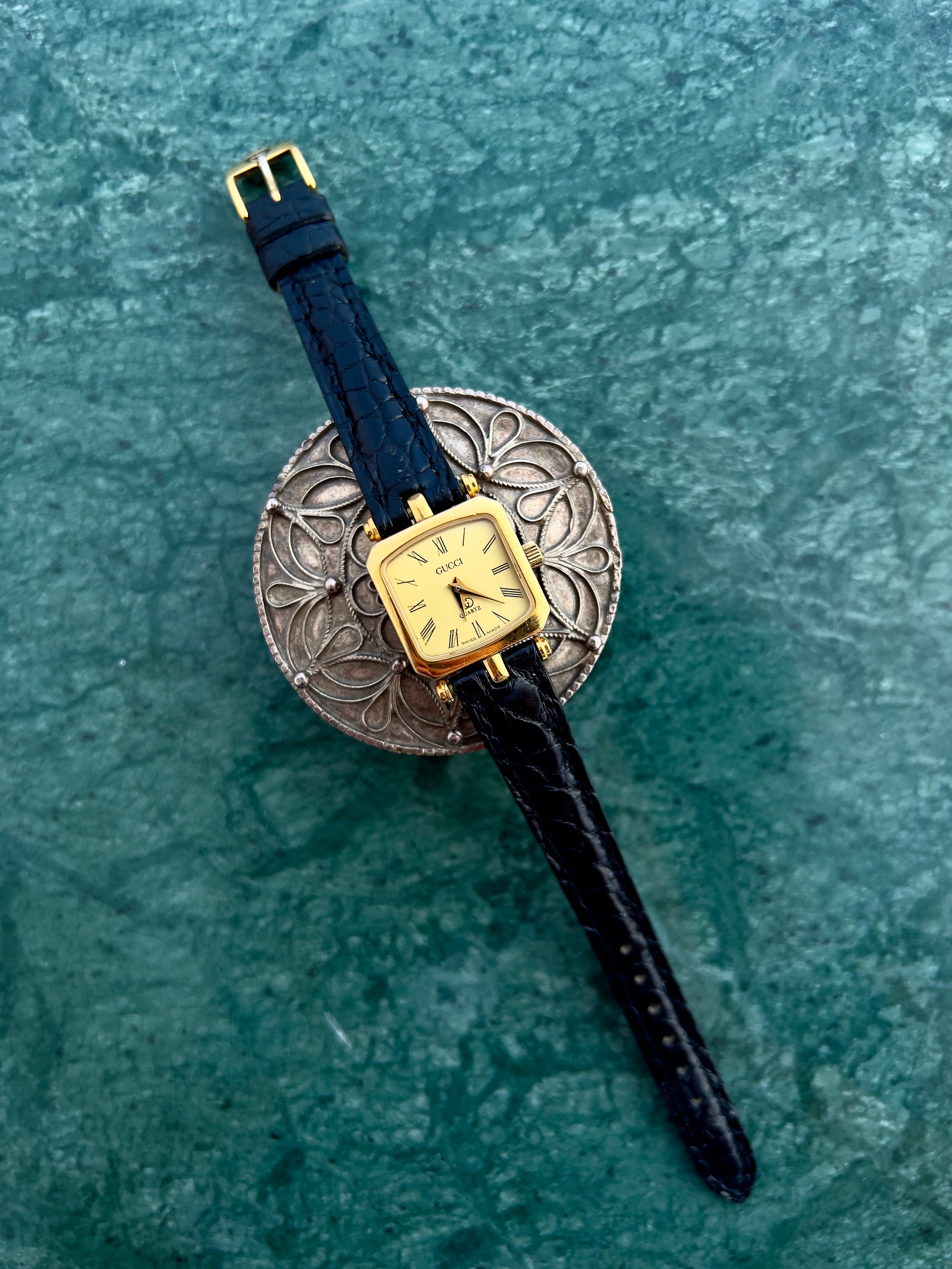 Gucci Wristwatch with gold case and black strap on a textured green surface