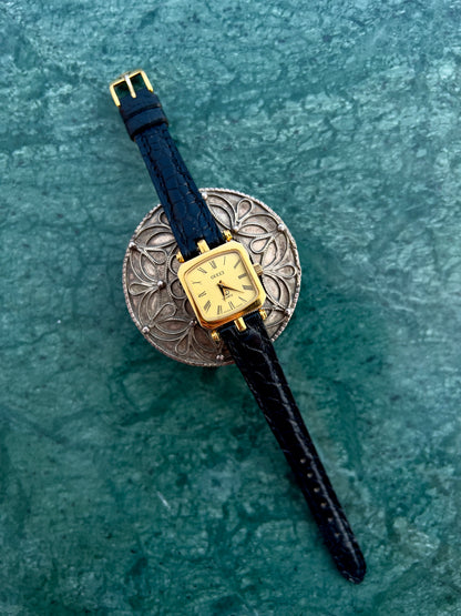 Gucci Wristwatch with gold case and black strap on a textured green surface