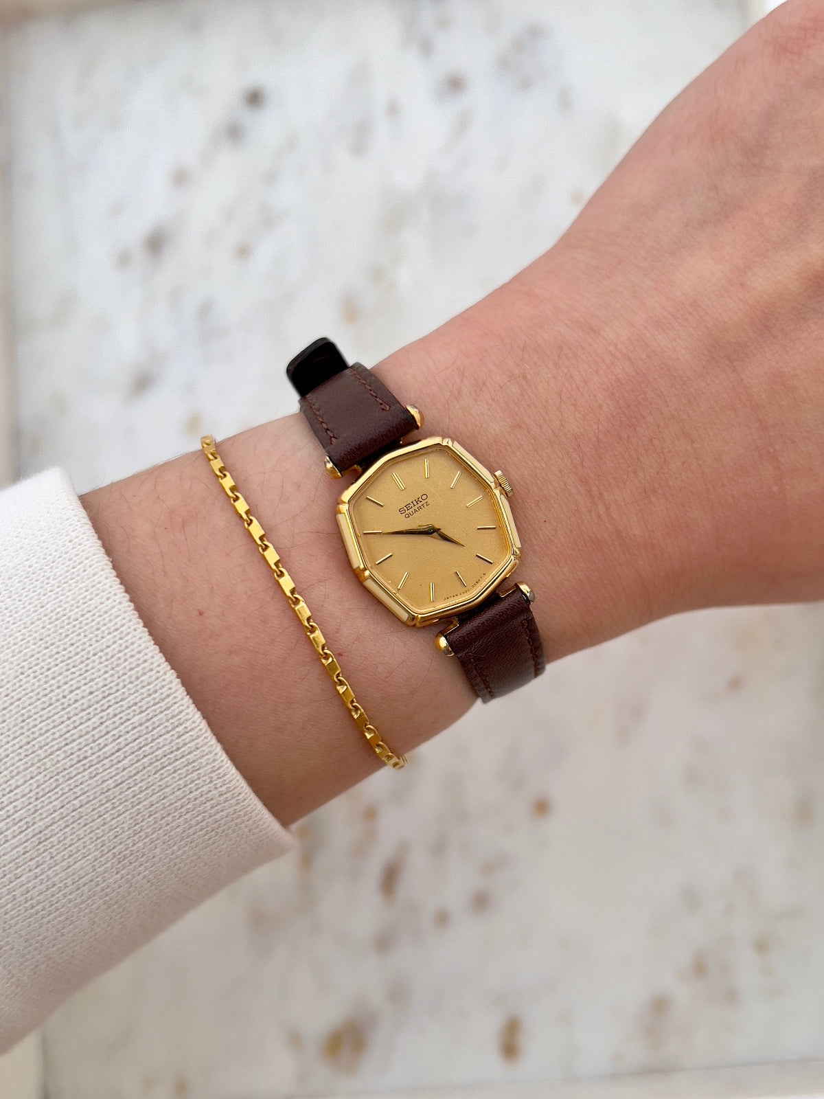 Seiko Gold women's watch with brown leather strap on wrist against a neutral background