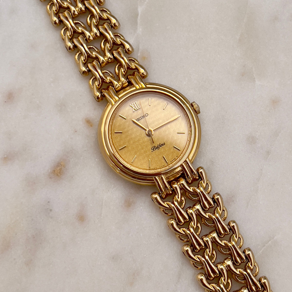 Seiko Belfina gold wristwatch with chain strap on a marble surface
