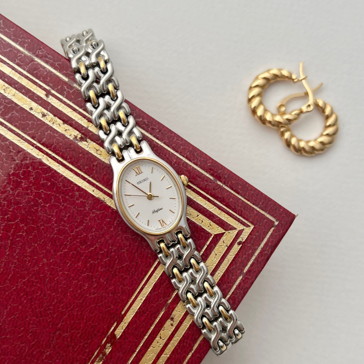 Seiko Belffina watch and gold hoop earrings on a red book with gold trim