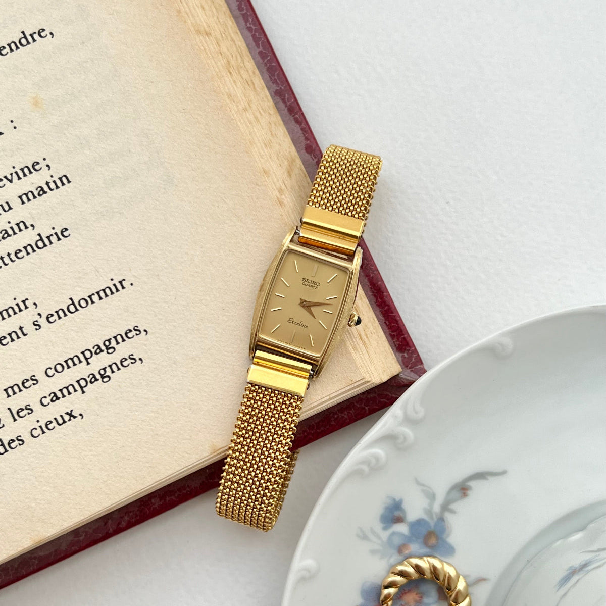 Seiko Gold women's watch on an open book with a decorative plate in the background