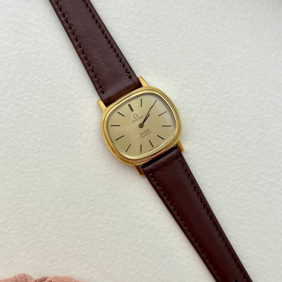 Omega De Ville Gold watch with a brown leather strap on a light textured surface