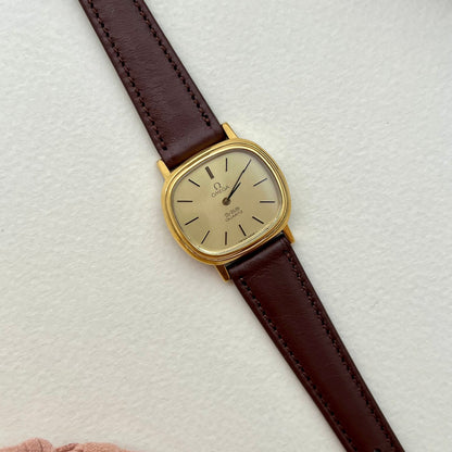 Omega De Ville Gold watch with a brown leather strap on a light textured surface