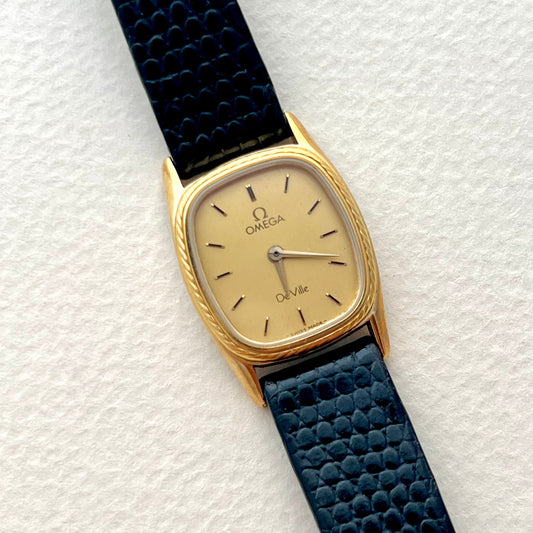 Gold Omega Woman's watch with a blue strap on a white background