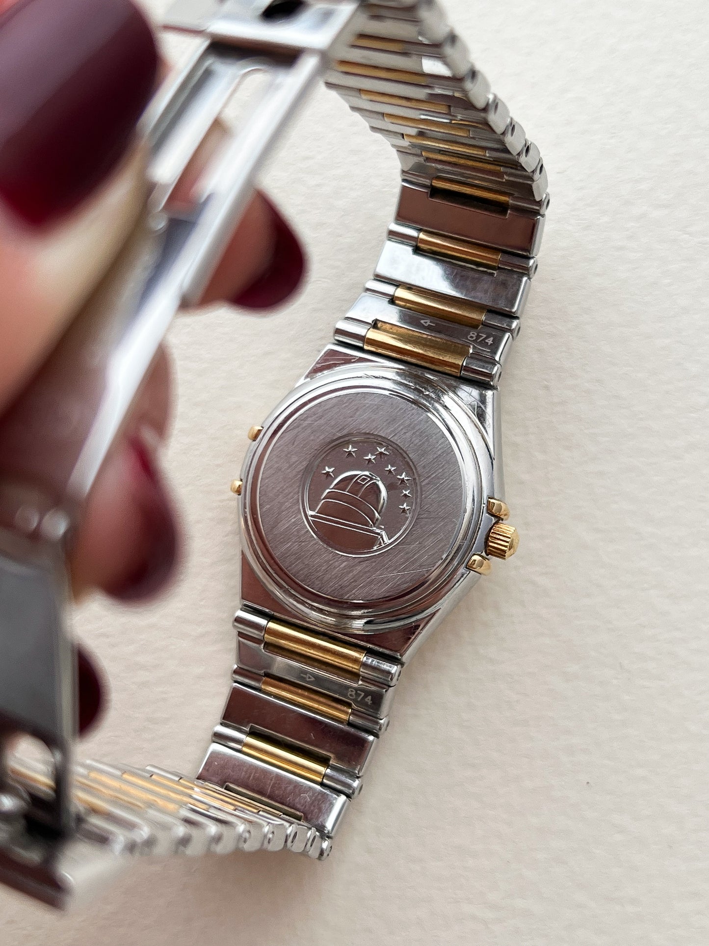 The Omega Constellation Manhattan Two Tone Women's Watch Caseback Emblem Close-up of a silver and gold watch with a visible brand logo on a light background