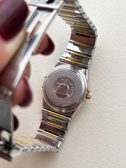 The Omega Constellation Manhattan Two Tone Women's Watch Caseback Emblem Close-up of a silver and gold watch with a visible brand logo on a light background