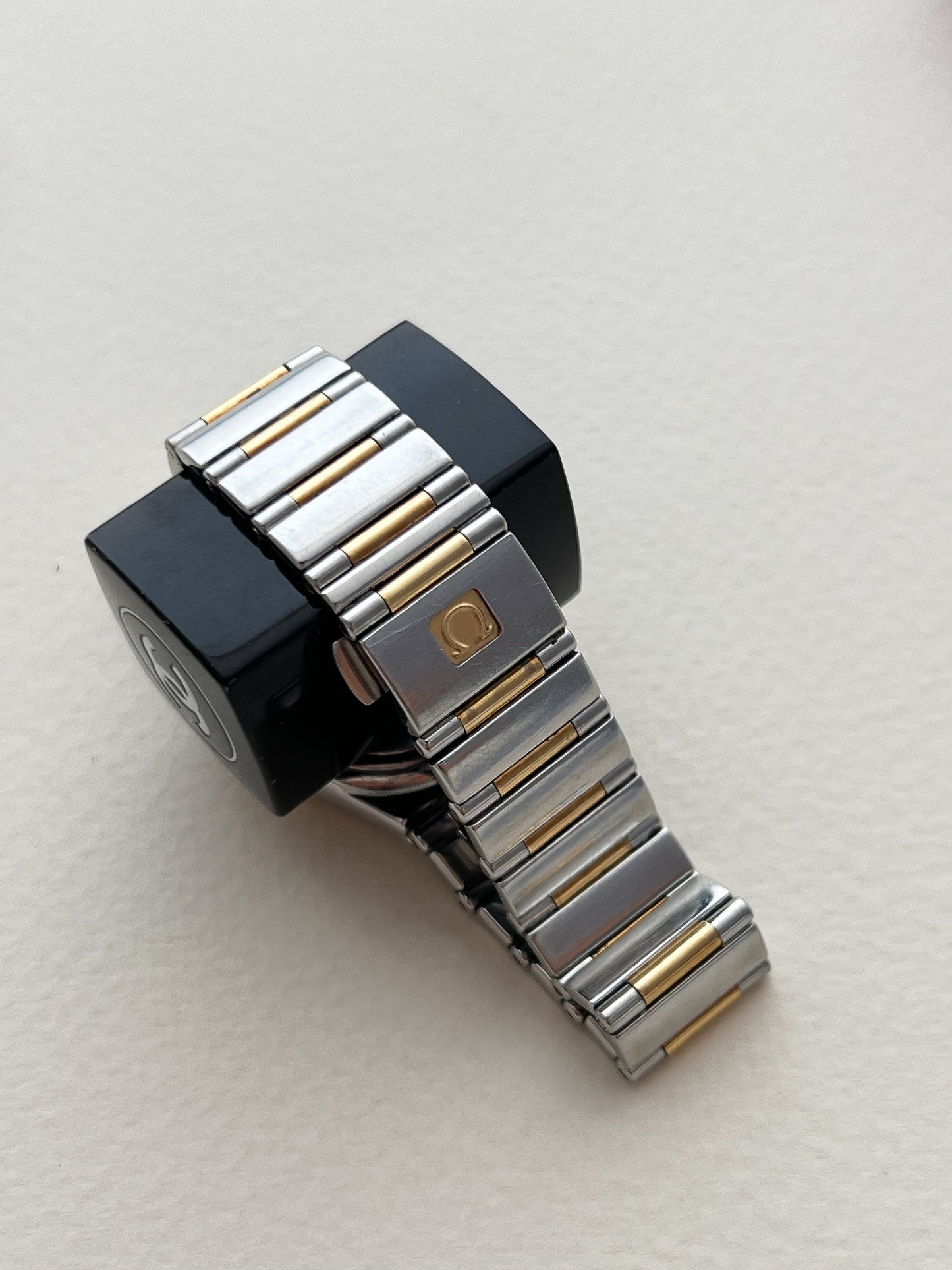Omega Constellation Bracelet Clasp Metallic watch strap with black end piece on a light beige background