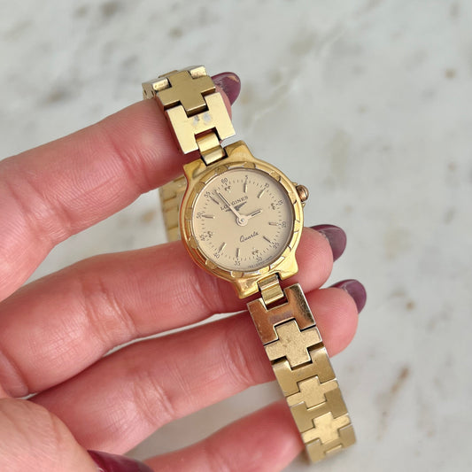 Gold watch held by a hand with a blurred background