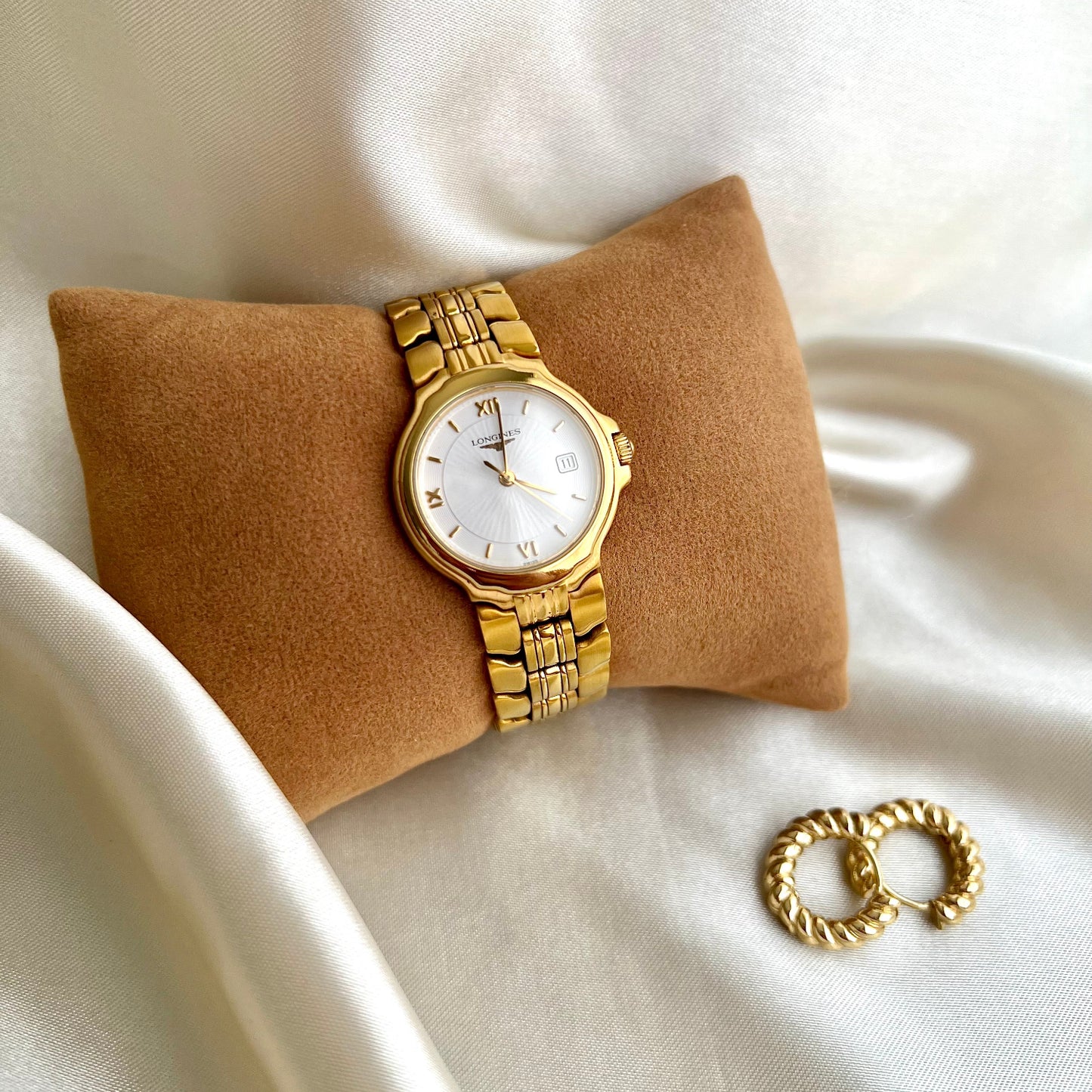 Gold Longines Conquest Women's watch and bracelet on a beige pillow with a white background
