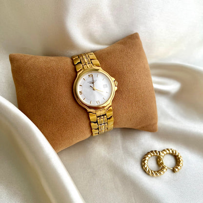 Gold Longines Conquest Women's watch and bracelet on a beige pillow with a white background