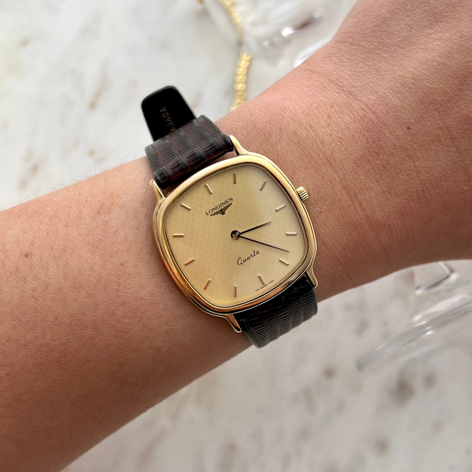 Gold watch with a black strap on a wrist against a light background
