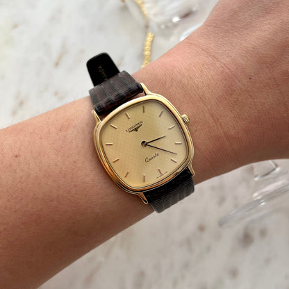 Gold watch with a black strap on a wrist against a light background