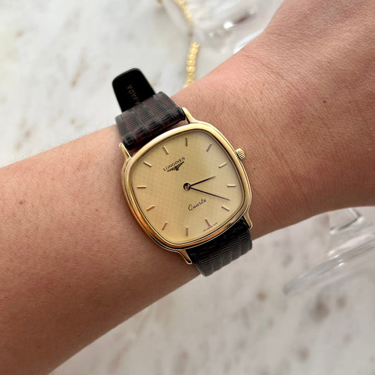 Gold watch with a black strap on a wrist against a light background