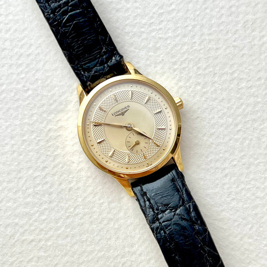 Longines Gold Round Women's wristwatch with a subseconds & guilloched dial black leather strap on a textured white background