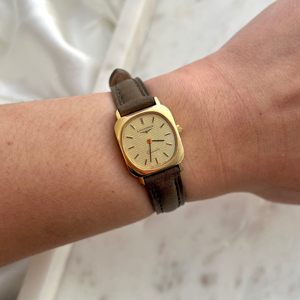 Longines gold watch with brown leather strap on a wrist against a white background