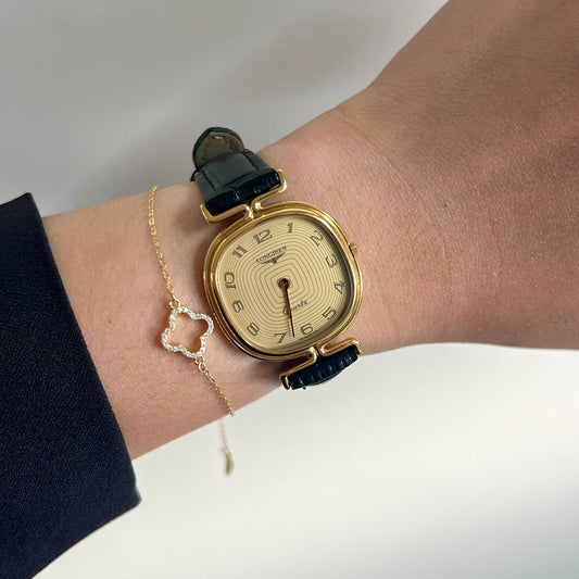 Longines gold wristwatch with black strap on a wrist against a neutral background