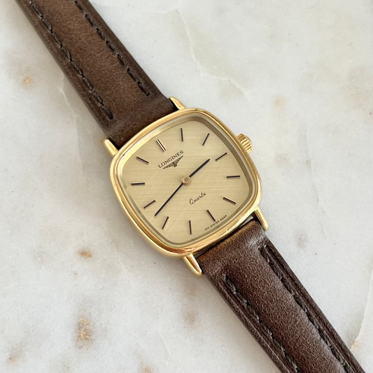 Vintage watch with brown leather strap and gold case on a light marble background