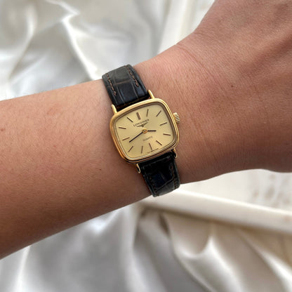 Gold watch with black leather strap on a wrist against a white fabric background