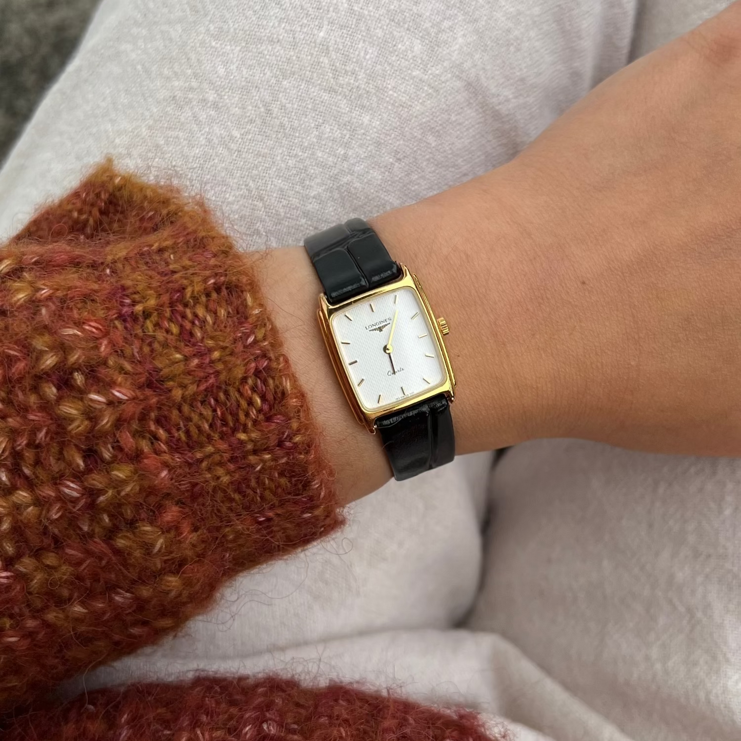 Person wearing a Longines gold women's watch with a black strap on a white background