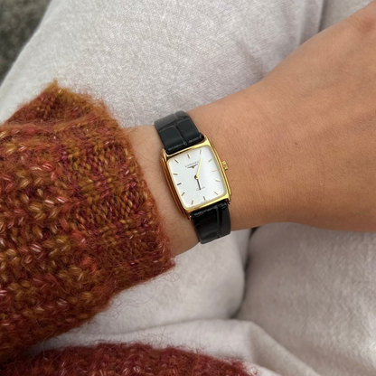 Person wearing a Longines gold women's watch with a black strap on a white background