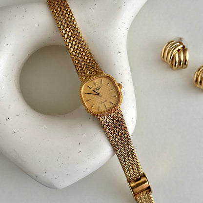 Gold Longines textured watch and earrings on a white stone surface