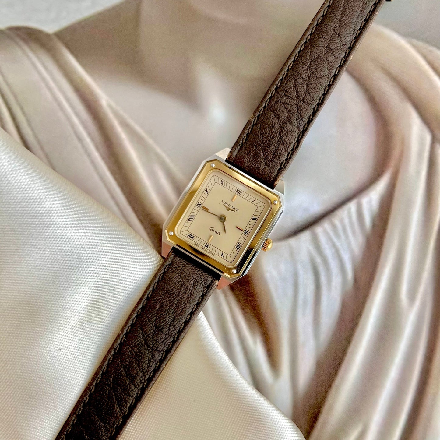 Vintage Longines Two Tone Women's watch with brown leather strap on a mannequin with a beige fabric background