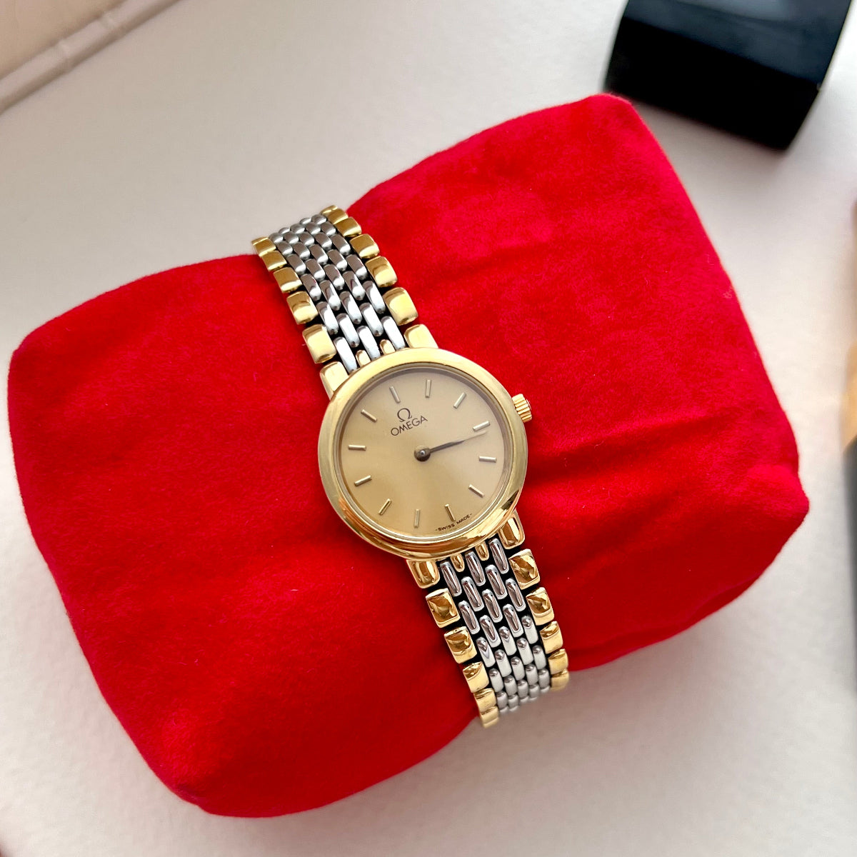 Gold Omega women's  watch with a silver bracelet on a red cushion