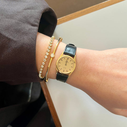 Omega Women's Gold watch NZ and bracelets on a wrist with a neutral background