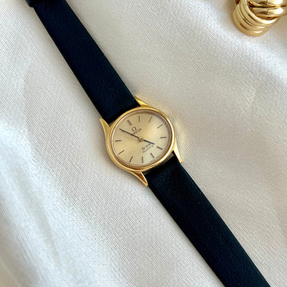 Omega De Ville Gold watch with black strap on a white fabric background