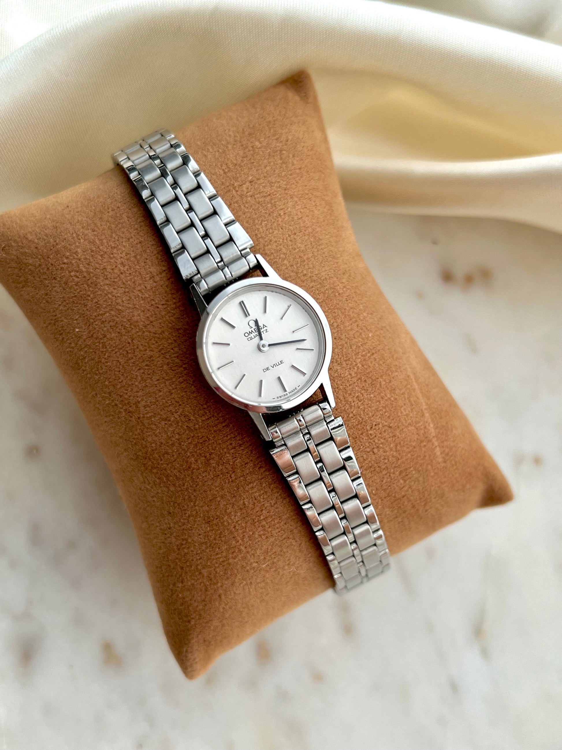 Omega De Ville Silver watch on a brown cushion with a marble background