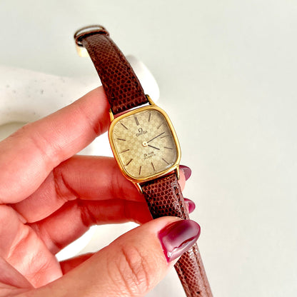 Vintage Omega De Ville Women's watch with brown strap held by a hand on a white background
