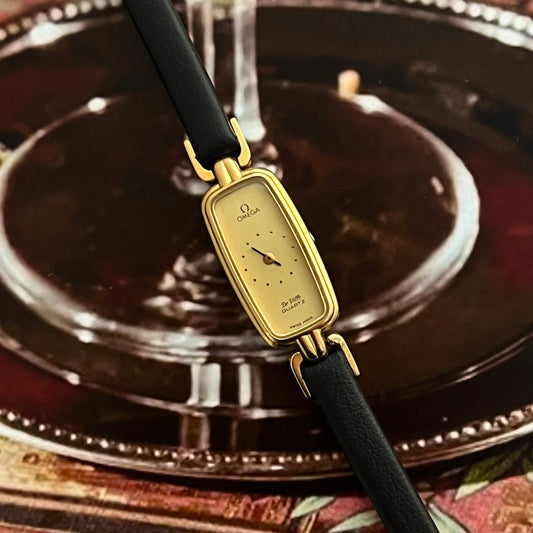 Gold Omega Women's watch with black strap on a decorative background