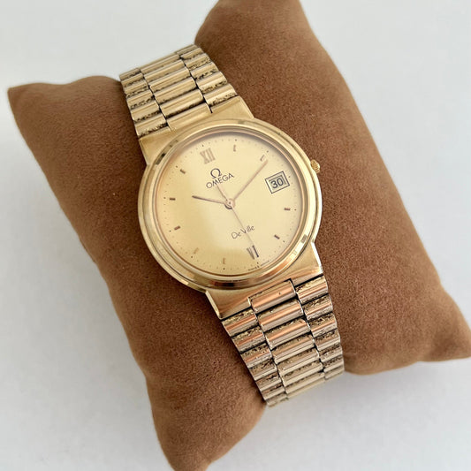 Omega Gold wristwatch on a brown cushion with a white background