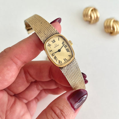 Omega Mechanical Gold wristwatch held by a hand with a white background