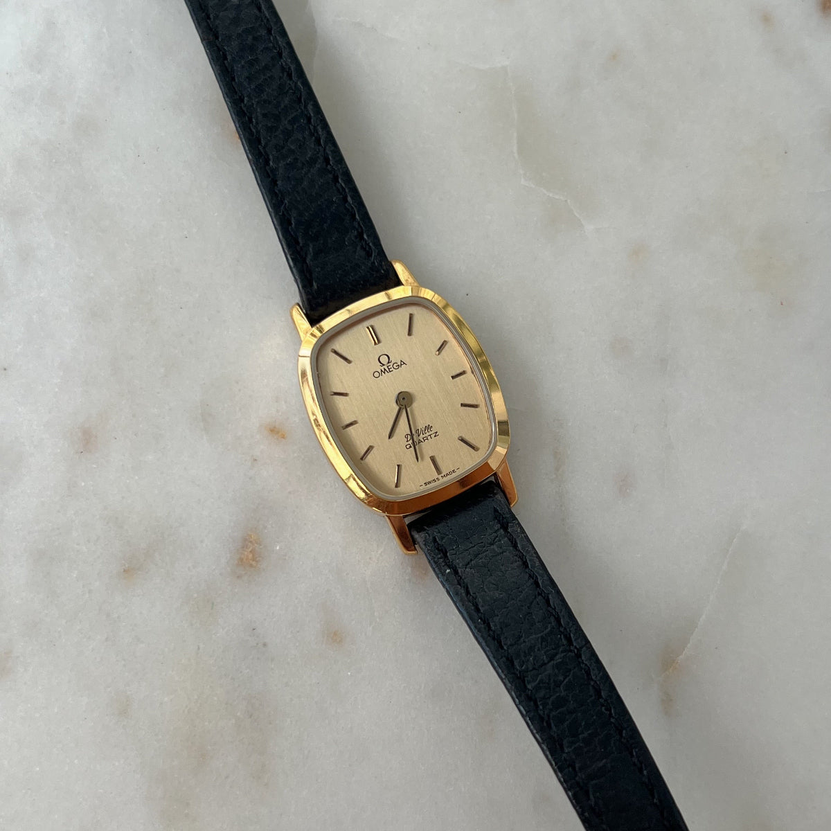 Omega Cushioned Women's watch with black strap and gold case on a marble surface