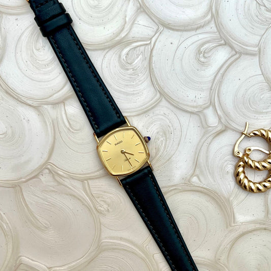 Rado Gold women's watch with black strap on a textured white surface