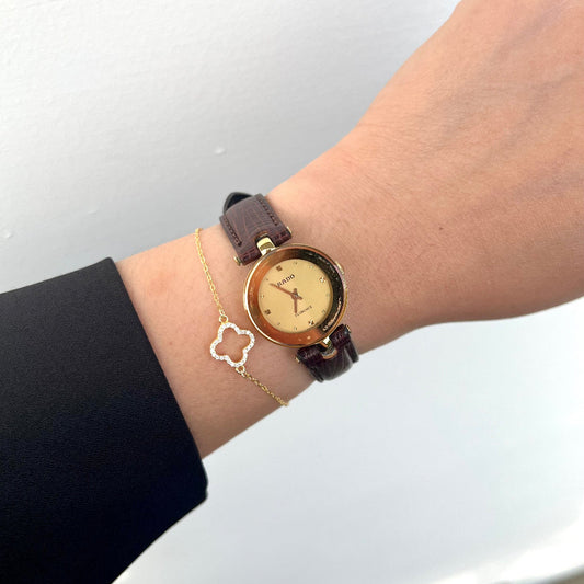 Hand wearing a gold  Rado ladies watch in NZ with a brown leather strap on a plain background